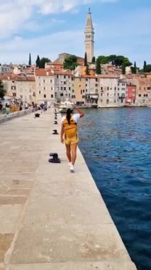 Sarı sırt çantalı bir gezgin, Rovinj 'in ışıldayan sularının kenarında sakin bir şekilde yürüyüp, tarihi binaların çarpıcı mimarisini ve canlı renklerini yakalıyor. Rovinj Hırvatistan