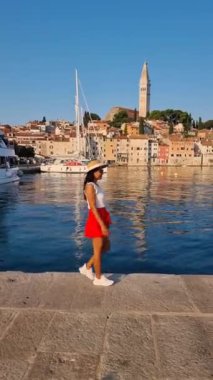 Genç bir kadın, Hırvatistan 'da açık mavi bir gökyüzünün altında büyüleyici mimari ve parıldayan suyla çevrili Rovinj' in pitoresk rıhtımında sakin bir yürüyüş yapıyor.
