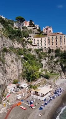 Büyüleyici Amalfi Sahili boyunca uzanan büyüleyici bir sahil koyunu keşfedin, canlı şemsiyeler, güneşlenenler ve güzel uçurumlar. Sıcak güneş bu huzurlu kaçışı aydınlatıyor..