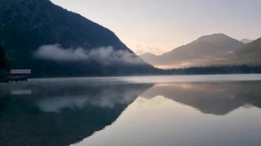 Plansee Avusturya 'da sakin bir göl üzerinde sabah, etrafındaki tepeleri ve yukardaki yumuşak bulutları yansıtıyor. Doğa bu nefes kesici manzarada uyanır.