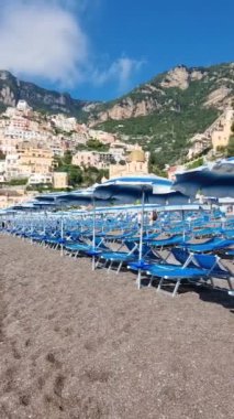 Ziyaretçiler, Positano 'da canlı şemsiyeler ve nefes kesici uçurumlarla çevrili güzel bir sahilde güneşli bir günün tadını çıkarıyorlar. Atmosfer davetkar ve deniz kenarında dinlenmek için mükemmel..