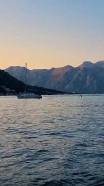Güneş dingin suların üzerinde batarken, bir yelkenli sersemletici dağ manzaraları arasında sorunsuzca süzülüyor. Sakin ortam, gün geceye dönerken rahatlama ve tefekküre davet eder. Kotor Körfezi Karadağ