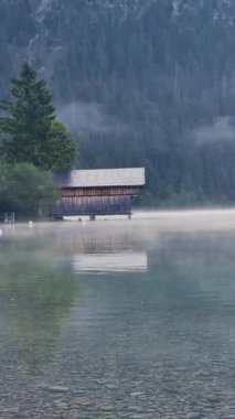 Sakin gölün yanında sakin bir kulübe duruyor, sabah sisi ile kaplanmış. Etrafındaki ağaçlar suya yansıyarak sakin bir atmosfer yaratıyor. Rahatlamak ve doğa severler için mükemmel Plansee Avusturya