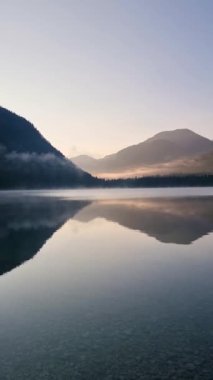 Şafak vakti, sakin göl çarpıcı dağ manzarasını yansıtırken, yumuşak sis suyun üzerine çöker ve barışçıl bir atmosfer yaratır. Plansee Avusturya