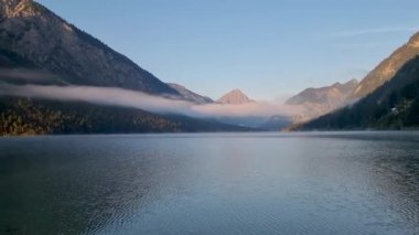 Sabah ışığı, Plansee Avusturya 'daki huzurlu bir dağ gölünün üzerine altın bir parıltı saçıyor. Sis etrafındaki tepeleri sarar ve sakin bir atmosfer yaratır. Bu manzarada doğa güzelliği gözler önüne seriliyor..