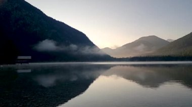 Huzurlu bir dağ gölünde şafağın dindirici güzelliğini hissedin. Sis kıyı şeridini sarıyor. Yumuşak yansımalar su yüzeyinde dans ederken, Plansee Avusturya