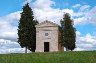 Tuscany 'deki yuvarlanan tepelerin arasında, uzun selvi ağaçları ve canlı mavi gökyüzü tarafından çerçevelenmiş, ziyaretçileri dingin güzelliğini ve zengin tarihini keşfetmeye çağıran, zamansız bir şapel duruyor..