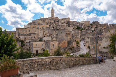 Matera 'nın tarihi kaldırım taşlarından geçen ziyaretçiler, dramatik bulutların ve mavi gökyüzünün altında taşa oyulmuş büyüleyici mimariye hayret ediyorlar..