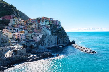 Parlak renkli evler Cinque Terre 'nin kayalıklarına yapışıp parlak mavi sulara ve kayalık kıyılara bakıyor. Ziyaretçiler Cinque Terre İtalya 'nın büyüleyici köyü Manarola' yı geziyorlar.