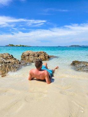 Samae San Adası 'nın el değmemiş sahillerinde, bir erkek ziyaretçi pürüzsüz kayaların yanında uzanırken sıcak güneşin tadını çıkarıyor. Kristal berrak sular ve yumuşak kumlar Tayland 'da keyifli bir geri çekilme yaratır..