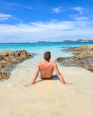 Samae San Adası, Tayland 'ın rahatlatıcı sularının tadını çıkaran bir adam kumlu sahilde güneşlenirken güneşlenir. Açık mavi deniz bitmeden uzanıyor, mükemmel bir kaçış yolu yaratıyor..