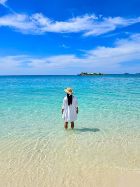 Yumuşak dalgalarda duran bir figür, parlak mavi gökyüzünün altındaki Samae San Adası 'nın berrak sularının tadını çıkarıyor. Bu huzurlu ortam ziyaretçileri doğanın güzelliğini ve huzurunu kucaklamaya davet ediyor..