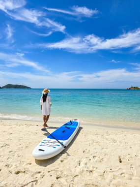 A serene moment unfolds as a woman stands on the sandy beach of Samae San Island, Thailand, gazing at the stunning turquoise waters. The sun shines brightly, creating a perfect day for adventure. clipart