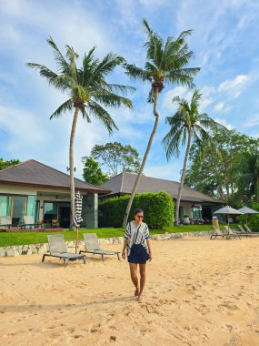 Strolling along the sandy beach of Bangsaray in Thailand, surrounded by lush greenery and swaying palm trees. clipart