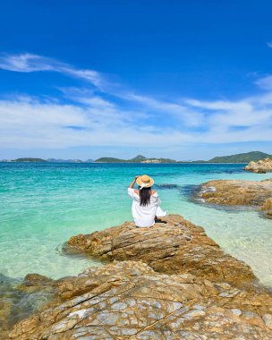 Enjoy a tranquil moment on the rocky shoreline of Samae San Island, Thailand. The clear turquoise waters shimmer under the bright sun, inviting relaxation and contemplation amidst a stunning backdrop. clipart