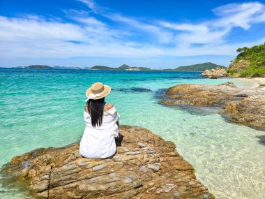 Basking in the sun on Samae San Island, a serene spot in Thailand, a visitor enjoys the stunning views. The crystal-clear waters and rocky shore create a peaceful atmosphere, perfect for relaxation. clipart