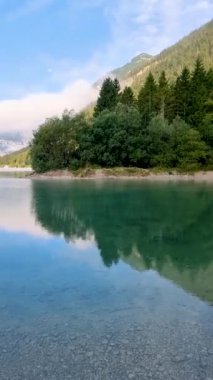 Yeşillik ve görkemli dağlarla çevrili sakin bir gölün güzelliğini keşfedin. Sakin su, dingin manzarayı yansıtıyor. Rahatlamaya davet eden sakin bir atmosfer yaratıyor..