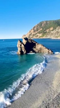 Dalgalar yavaşça kumlu bir kıyıya vurarak turkuaz sulara çarpan çarpıcı bir kaya oluşumunu ortaya çıkarıyor. Monterosso Cinque Terre İtalya