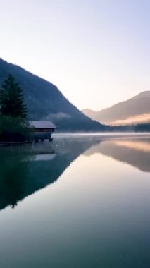 Sabahın erken saatlerinde sakin suların heybetli dağları ve rahat ahşap bir kulübeyi yansıtan çarpıcı bir manzarası ortaya çıkar. Doğa yumuşak bir ışık ve yumuşak bir sis ile uyanıyor, barışçıl bir atmosfer yaratıyor..
