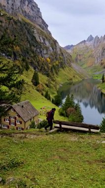 Yalnız bir gezgin, görkemli dağlar ve sonbahar renkleriyle çevrili yansıtıcı bir göl kenarında manzaralı bir patika boyunca yürür. Falensee İsviçre