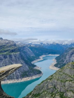Nefes kesen bir manzara, engebeli dağları kesen kıvrımlı bir nehri ortaya çıkarır. Uzakta kar parçaları parlar. Trolltunga Norveç