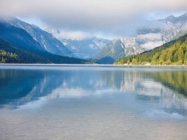 Huzurlu bir göl, görkemli dağları ve bereketli ormanı sabah ışığı altında yansıtır. Sakin su nefes kesen manzarayı mükemmel bir şekilde yakalıyor, sükunet hissi uyandırıyor. Plansee Avusturya