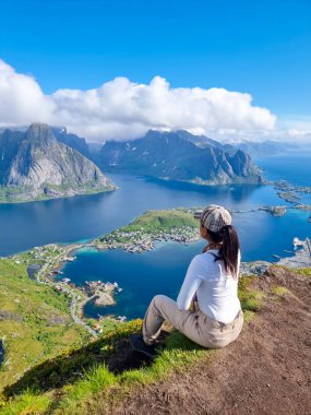 Lofoten Norveç 'teki bir uçurumun kenarında oturan bir yürüyüşçü, açık mavi gökyüzünün altındaki Kuzey Norveç' in büyüleyici fiyortlarına ve adalarına hayran.. 