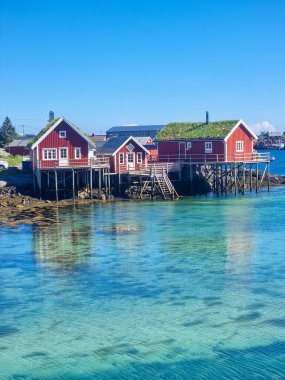 Huzurlu bir sahil şeridi ile süslenmiş, durgun renkli evler berrak, turkuaz suları yansıtıyor, Lofoten Norveç 'in bu pitoresk sahil köyünde huzur hissi uyandırıyor.