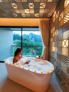 Huzuru kucaklayan bir insan, yumuşak mumlarla aydınlatılmış kabarcıklarla dolu şık bir küvette dinlenir. Alacakaranlık çökerken yemyeşil tepelerin büyüleyici görüntüsü güzel bir şekilde yankılanıyor..