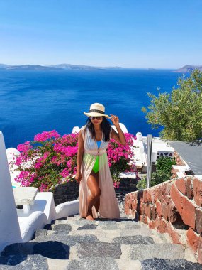Bir gezgin Santorini 'deki resimsel taş basamaklardan inerken parlak pembe bougainvillea derin mavi denizle çok güzel zıtlaşır. Sıcak güneş, cennet gibi yaz gününü güzelleştirir..
