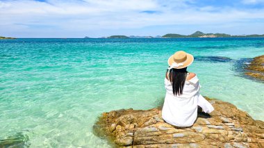 A serene day unfolds on Samae San Island as a woman enjoys the stunning turquoise waters. She sits peacefully on a rocky outcrop, basking in the warmth of the sun and the beauty around her. clipart