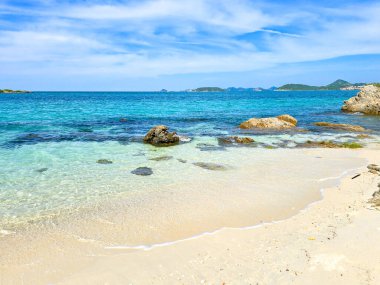 Crystal-clear waters wash gently onto the soft sand of Samae San Island, inviting visitors to relax under the sun. Rocky formations dot the landscape, adding to the island's natural beauty and charm. clipart