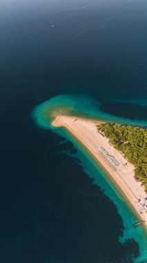 Altın kumlar, Brac Adası 'ndaki Zlatni Rat plajında yemyeşil yemyeşil tarafından kucaklanan canlı mavi denize doğru uzanıyor. Ziyaretçiler sıcak güneş ve yumuşak dalgaların altında sakin bir atmosferin keyfini çıkarıyorlar. Hırvatistan