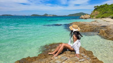 Bright sunlight casts a warm glow on the pristine shores of Samae San Island, where a serene figure enjoys the stunning turquoise waters. Waves gently lap at the rocks, creating a tranquil escape. clipart