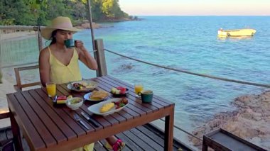 Koh Munnork Adası 'nda huzurlu bir sabahın tadını çıkarın canlı meyveler ve taze içeceklerle lezzetli bir kahvaltı yaparken turkuaz okyanusu ve yakındaki tekneyi seyredin..