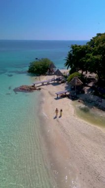 Tayland 'daki Koh Munnork Adası' nın nefes kesici kıyılarını keşfedin. Ziyaretçiler yumuşak kum ve turkuaz sularda gezinirken. Bir çift, bu gizli cennetin huzur ve doğal cazibesinin tadını çıkarıyor..