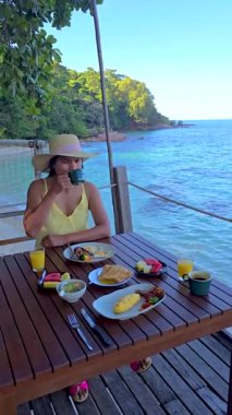 Koh Munnork, turkuaz sularda kahvenin tadını çıkar. Tropikal tatları ve sakin bir atmosferi tecrübe edin. Okyanusta kahvaltı yapan Asyalı bir kadın.