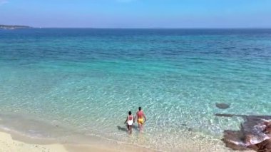 Tayland 'daki Koh Munnork Adası' nın güzelliğini keşfedin. Turkuaz sular sizi sahil boyunca sakin bir gezintiye davet ediyor. Sahilde okyanusta dinlenen farklı bir çift kadın ve erkek.