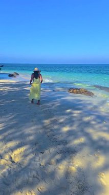 Koh Munnork Adası 'nın yumuşak kumlu sahillerinde dolaşın, açık mavi gökyüzünün altında güneşi emerek. Okyanusta dinlenen Asyalı kadınlar, şapkalı sarı elbiseli bir kadın.