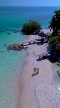 Koh Munnork Adası 'nın yumuşak kumları boyunca, canlı suların yemyeşil ile buluştuğu Tayland, Rayong' da sakin bir gezinti yapın. Bir çift adam ve kadın sahilde yürüyorlar.