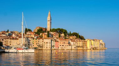 Güneş Rovinj Hırvatistan 'ın üzerinde batarken, gökyüzü sıcak renklerle boyanmış ve güzel rıhtımda altın bir parıltı bırakmıştı. Huzurlu yelkenlilerin eşlik ettiği renkli binalar kıyı boyunca uzanır. 