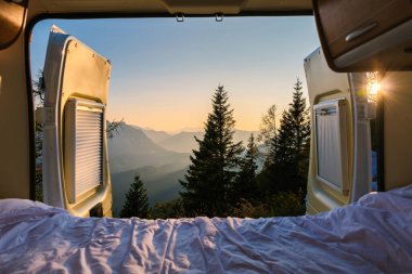 Avusturya 'nın Avusturya Alpleri' nde nefes kesen bir dağ manzarasını gözler önüne seren güneşli bir sabah, bir kamp aracının açık kapılarından içeri doğru akmaktadır. Doğa altın renklerde uyanır..