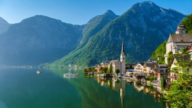 Yükselen tepeler arasında, gölün üzerindeki resim gibi bir köy berrak mavi gökyüzünü yansıtıyor, Hallstatt Avusturya