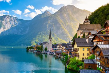 Görkemli dağların arasına gizlenmiş Avusturya Hallstatt mimarisi sakin göl boyunca altın güneş ışığını gün sona ererken yansıtıyor. Büyüleyici bir an bekliyor..
