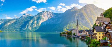 Görkemli dağların arasında, Hallstatt 'ın pitoresk köyü güneşin altın ışınlarının altında uyanır, Avusturya' daki dingin göle canlı yansımalar yansıtır.