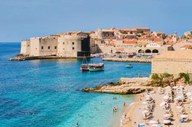 Ziyaretçiler yaz boyunca sıcak güneş ve temiz suyun keyfini çıkarırken, dalgalar yavaşça Dubrovnik Hırvatistan 'ın kumlu kıyılarına çarpıyor