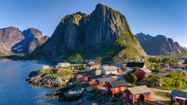 Norveç 'te engebeli dağların ve sakin mavi fiyortların arasına yerleşmiş kırmızı kulübelerin yer aldığı küçük bir köyün pitoresk bir manzarası. Yazın Hamnoy Lofoten Norveç