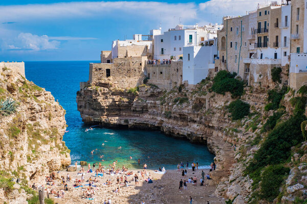 В очаровательном городе Полиньяно-а-Маре, Италия, посетители отдыхают на песчаных берегах посреди возвышающихся скал. Лазурные воды мешают и местным жителям, и туристам наслаждаться теплым солнцем и океаном