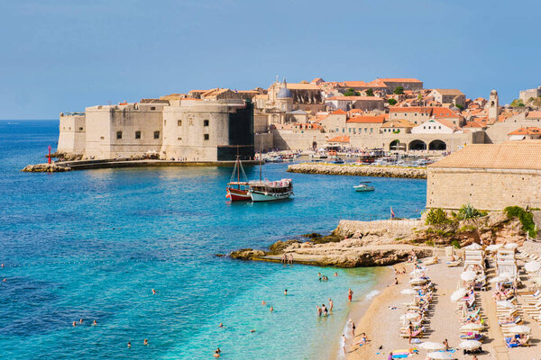 Волны мягко опускаются на песчаный берег Дубровника Хорватия, так как посетители летом наслаждаются теплым солнцем и чистой водой