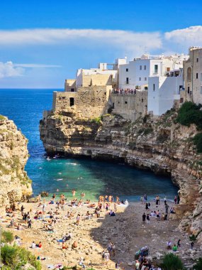 Polignano a Mare Vibrant beyaz binalar engebeli uçurumlara tutunur, sakin turkuaz sulara bakar. Ziyaretçiler güneşli ve güneşli bir günde İtalya 'nın Puglia kentindeki çarpıcı plajın tadını çıkarıyorlar..